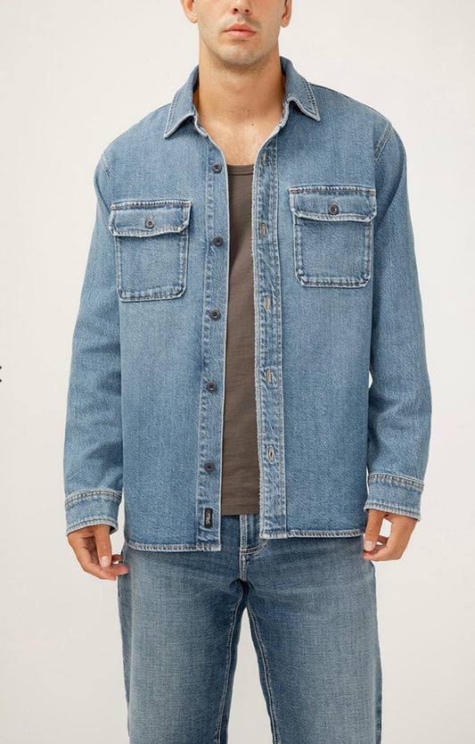 A man wearing the Silver Jeans Co. Men’s Denim Shirt Jacket in light blue over a gray shirt with matching blue jeans, standing against a plain light background.