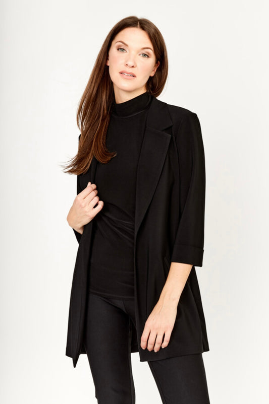 A woman with long brown hair models the Frank Lyman Long Open-Front Jacket in black (Style 236005) as a chic layering piece over a black turtleneck top and black pants, standing against a plain light background.