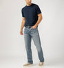 Dressed in a black t-shirt and Silver Jeans Co.'s Grayson Classic Fit Straight Leg Jeans, a person stands casually with a hand in their pocket. They sport gray sneakers against a plain light gray backdrop.
