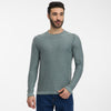 A man with short dark hair and a beard is wearing the TORIEN Mens Flat Knit Shirt by RAGWEAR in light green and blue jeans, standing against a plain white background, looking slightly to the side.