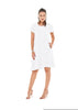 A woman with dark hair is posing in the LA DRESS SNOW by Oh My Gauze, a short-sleeve, white cotton gauze dress featuring cutout shoulder details that reaches just above her knees. She is wearing beige high-heeled sandals and has one hand in her dress pocket. The background is white.