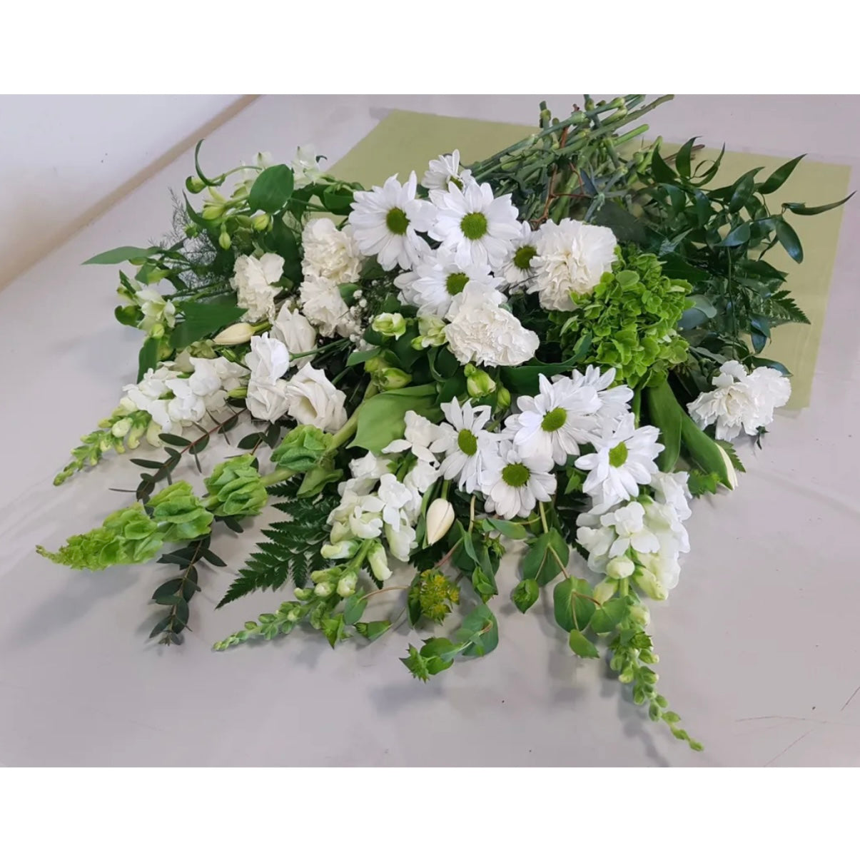 The Natures Bounty Fresh Cut bouquet by Posies Flowers & Fashion is elegantly arranged in a vase, featuring white daisies, carnations, snapdragons, and green leaves. This fresh and vibrant display is appropriate for any occasion.