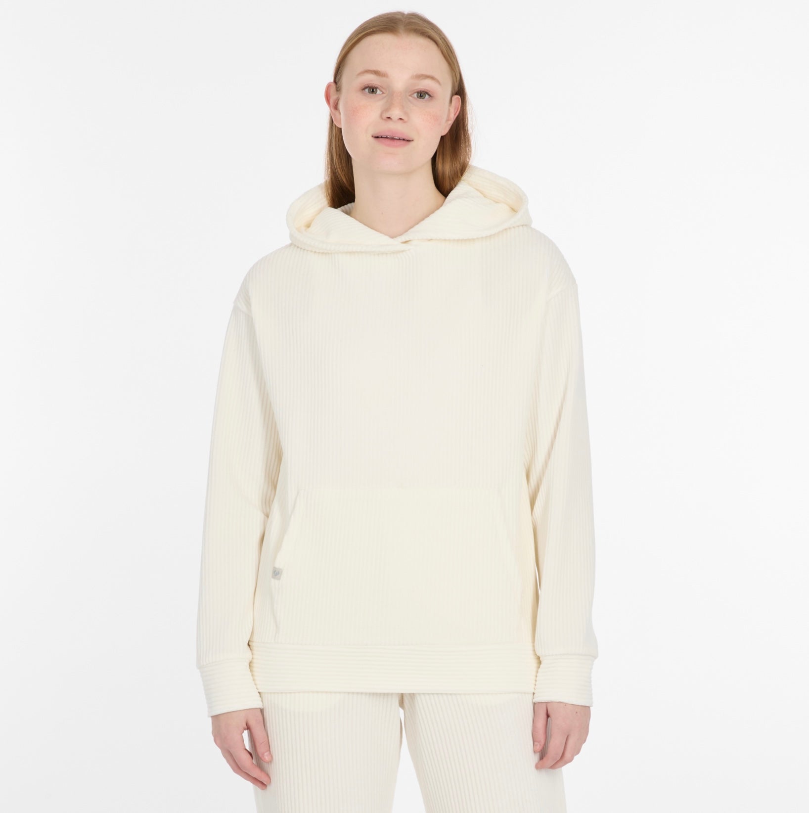 A person with straight blonde hair wears a cozy, off-white COLBIE CORDY Sweatshirt by RAGWEAR with matching pants, standing against a plain white background and smiling gently at the camera.