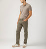 A person wearing a beige polo, Machray Athletic Fit Straight Leg Pants M63410LBS659 by Silver Jeans Co. in olive green, and white sneakers with brown accents stands against a light gray background, posing with one hand in their pocket and looking left.