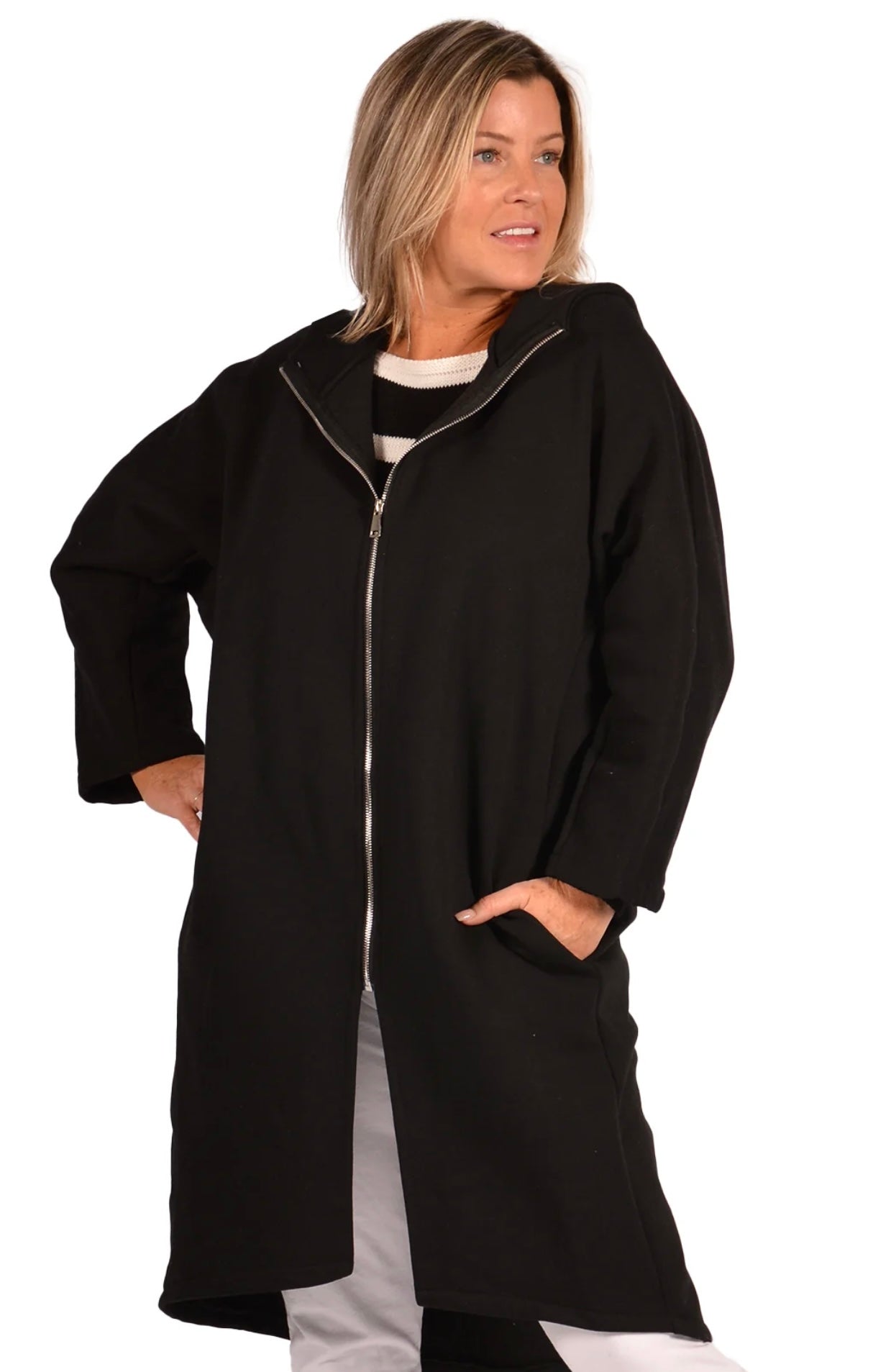 A woman with shoulder-length blonde hair is wearing a stylish Catherine Lillywhite BK LONG HOODIE COAT with a silver zipper. She has her hands in the coat pockets and is looking slightly to the side with a slight smile. She is also wearing a black and white striped shirt underneath.