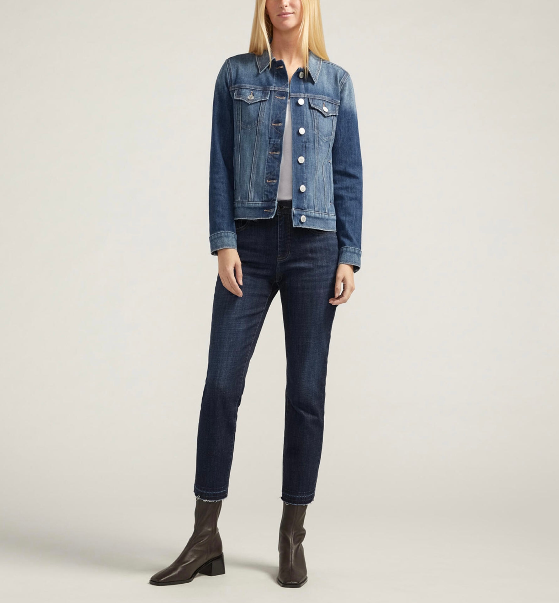 A person wearing the JAG Kiara Jean Jacket J8309DSS342 in a medium indigo wash and dark jeans stands against a neutral background. They pair this stylish denim jacket with brown ankle boots, creating a casually chic look.