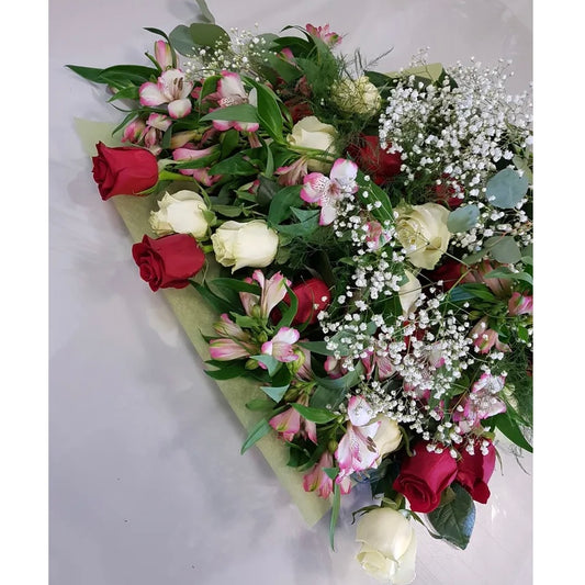 The Sweetheart Kisses Freshcut by Posies Flowers & Fashion features red and white roses, pink alstroemeria, white baby's breath, and lush greenery in a delicate vase on a light surface, illustrating the charm of fresh flowers.