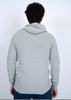 A person with dark hair, wearing HEDGE’s eco-friendly MENS HOODED SWEATER-OATMEAL MEL TWIST and blue jeans, stands with their back to the camera against a plain white background.