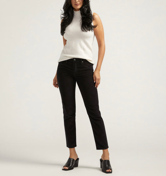 A person with long dark hair is wearing a sleeveless white turtleneck top, JAG's Cassie Mid Rise Slim Straight Leg Pants Corduroy (J2940VSC624) in black, and black open-toe shoes. They are standing against a plain light-colored background.