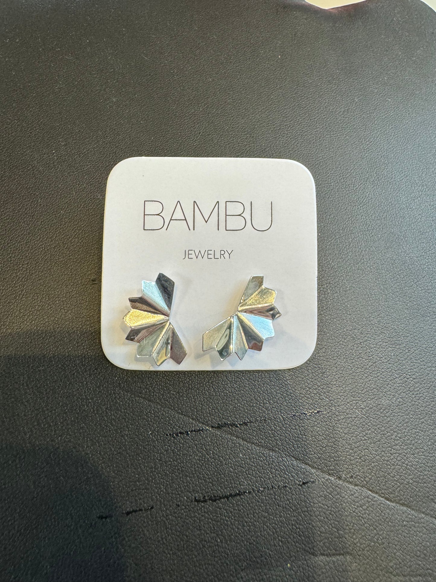 A pair of Silver Palm Fan - BAMBU earrings is displayed on a small, square white card with "BAMBU Jewellery" printed in the center. The earrings showcase a modern, angular design and rest on a dark surface, making them perfect for the eco-conscious fashionista.