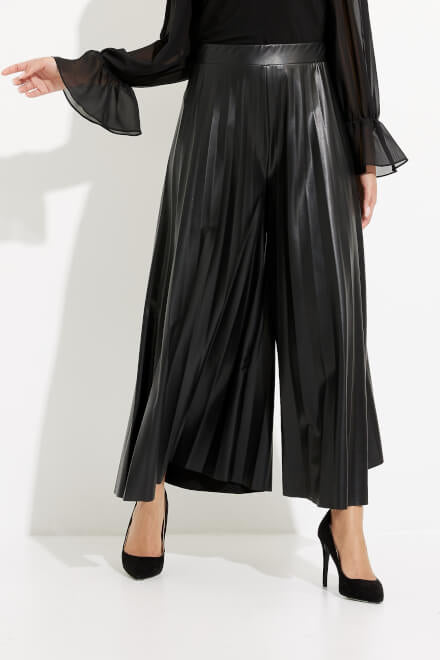 A person is wearing a pair of Joseph Ribkoff Wide Leg Culotte Pants Style 233109 in black. They are also wearing a black, long-sleeve blouse with sheer bell sleeves and black high-heeled shoes. The background is plain white.