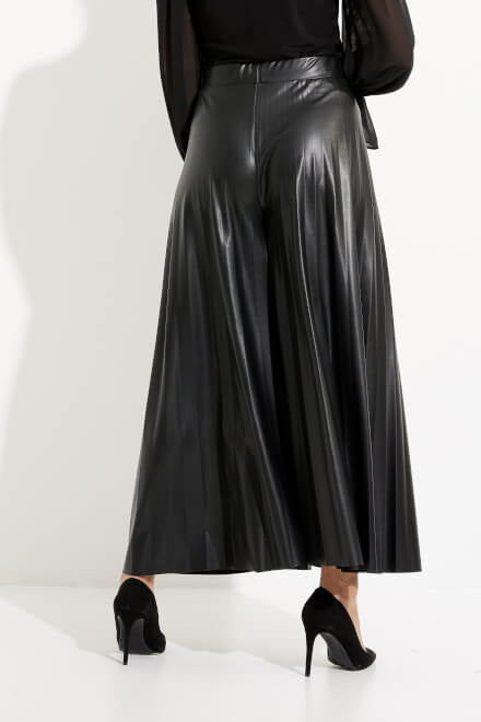 A person is wearing a pair of Joseph Ribkoff Wide Leg Culotte Pants Style 233109 in black. They are also wearing a black, long-sleeve blouse with sheer bell sleeves and black high-heeled shoes. The background is plain white.