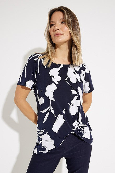 A woman with shoulder-length blonde hair, dressed in a navy and white Floral Print Tunic Style 231262 by Joseph Ribkoff, is looking up to her right. She pairs this stylish top with sleek pants. The background is plain white.