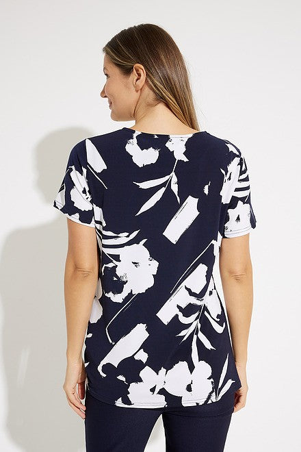 A woman with shoulder-length blonde hair, dressed in a navy and white Floral Print Tunic Style 231262 by Joseph Ribkoff, is looking up to her right. She pairs this stylish top with sleek pants. The background is plain white.