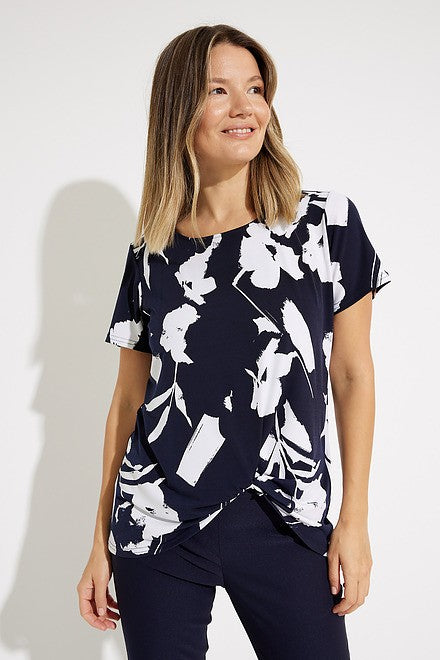 A woman with shoulder-length blonde hair, dressed in a navy and white Floral Print Tunic Style 231262 by Joseph Ribkoff, is looking up to her right. She pairs this stylish top with sleek pants. The background is plain white.