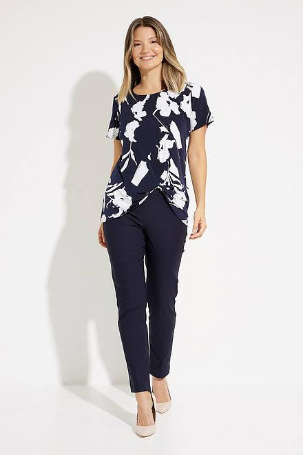 A woman with shoulder-length blonde hair, dressed in a navy and white Floral Print Tunic Style 231262 by Joseph Ribkoff, is looking up to her right. She pairs this stylish top with sleek pants. The background is plain white.