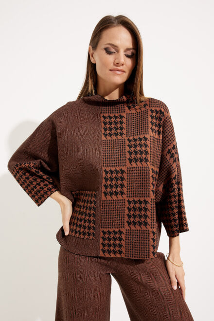 A woman with long hair wears the Houndstooth & Patchwork Sweater Style 233903 in brown and black from Joseph Ribkoff, featuring three-quarter sleeves and matching pants. She poses with her left hand on her hip, looking slightly downward with a relaxed expression. The white background highlights the intricate houndstooth detailing of her coordinated outfit.