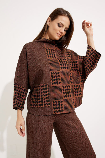 A woman with long hair wears the Houndstooth & Patchwork Sweater Style 233903 in brown and black from Joseph Ribkoff, featuring three-quarter sleeves and matching pants. She poses with her left hand on her hip, looking slightly downward with a relaxed expression. The white background highlights the intricate houndstooth detailing of her coordinated outfit.