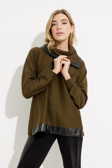 A person with blonde hair poses against a white background, wearing an olive/black Joseph Ribkoff Faux Leather Contrast Trim Style 233041 top. Their hands are gently clasped near their chest as they look towards the camera, paired with classic jeans.