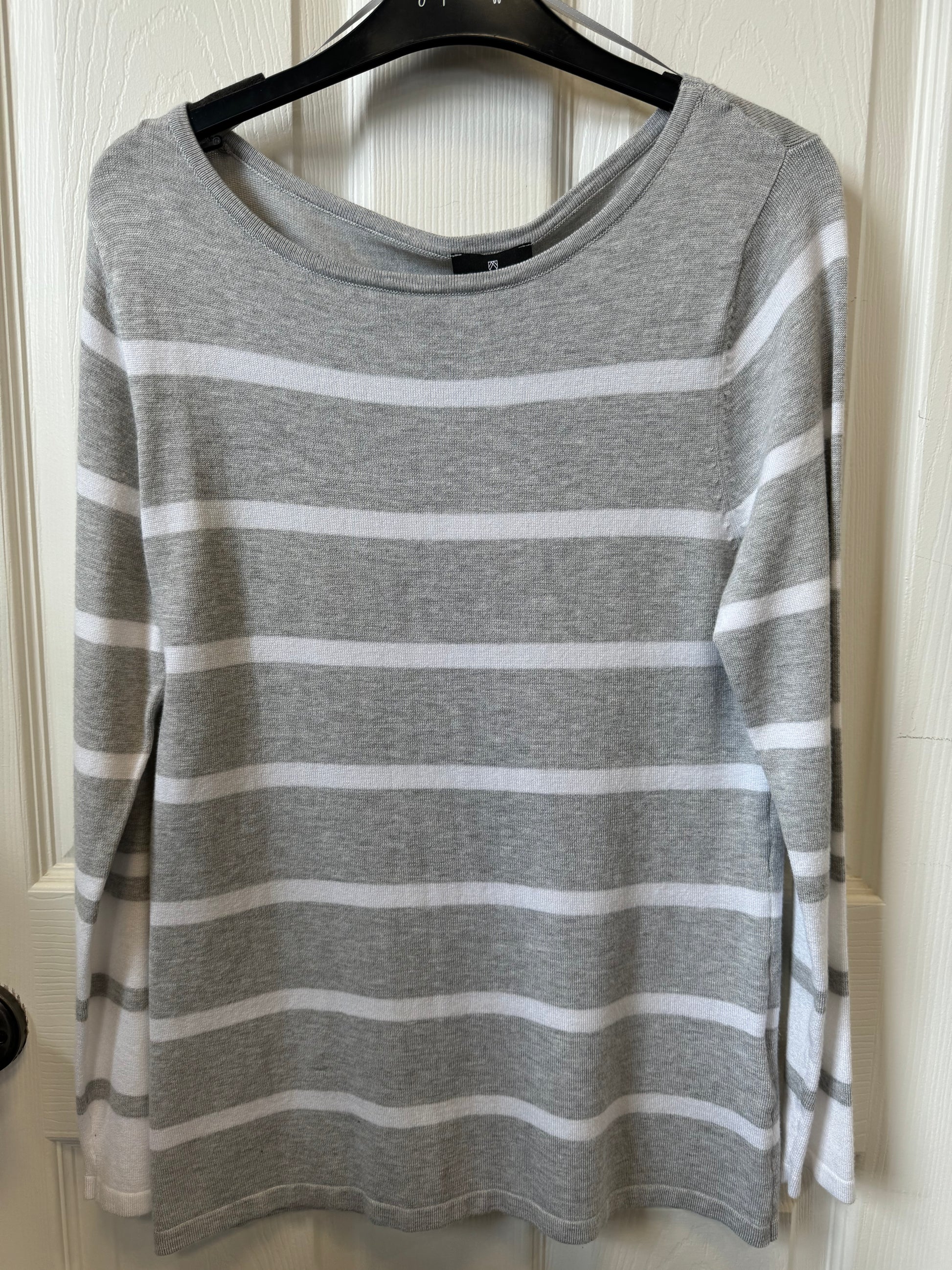 A MARBLE Grey/White Striped Fine Knit Sweater is displayed on a black coat hanger, hanging on a white door. This designer sweater features a round neckline and long sleeves.