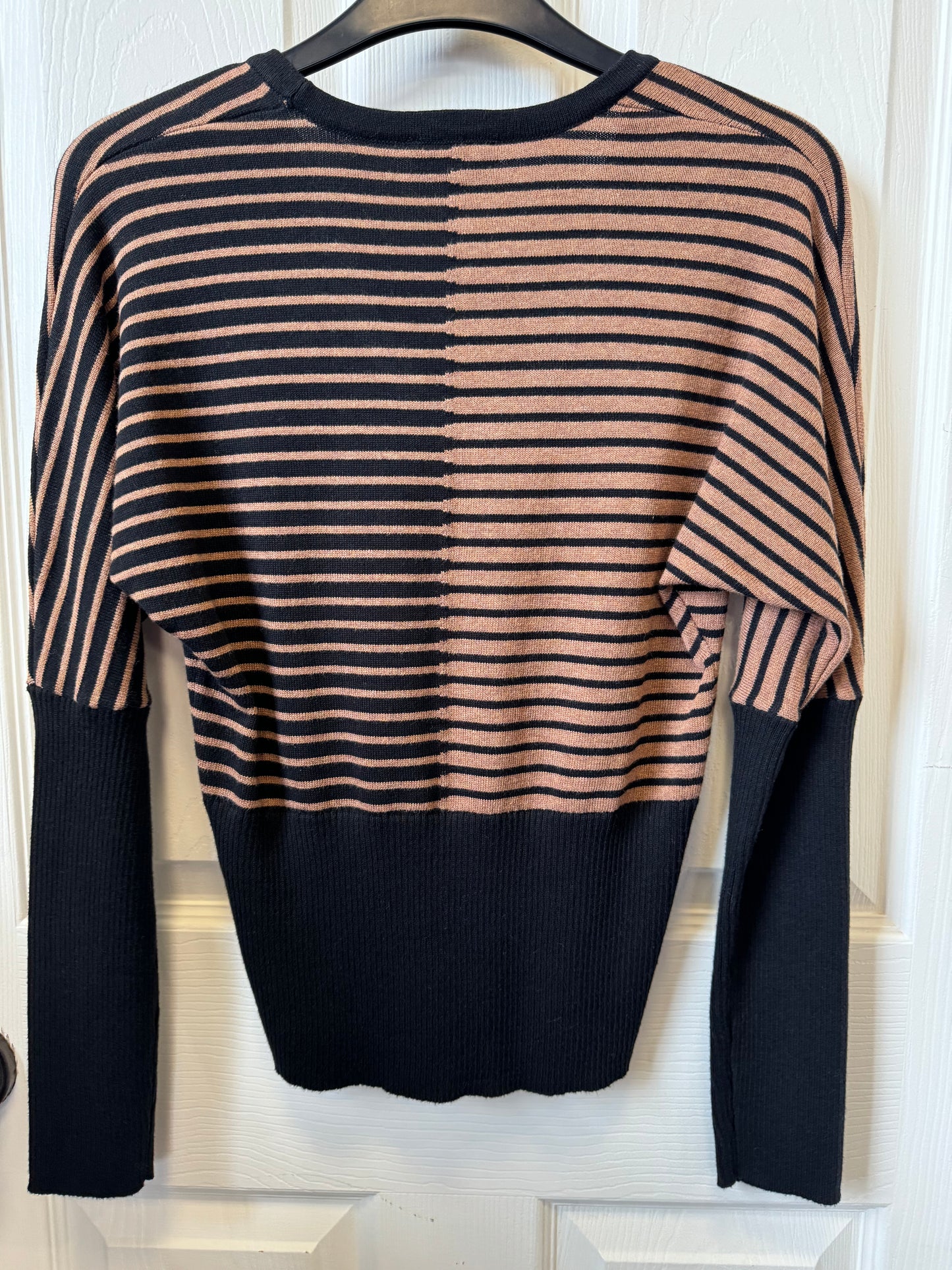 A Marble L/S Knit Tapered sweater by MARBLE hangs on a hanger against a white wooden background. The long-sleeved V-neck sweater features a black and tan stripe pattern on the top half and solid black from the chest down, including the sleeves' lower half.