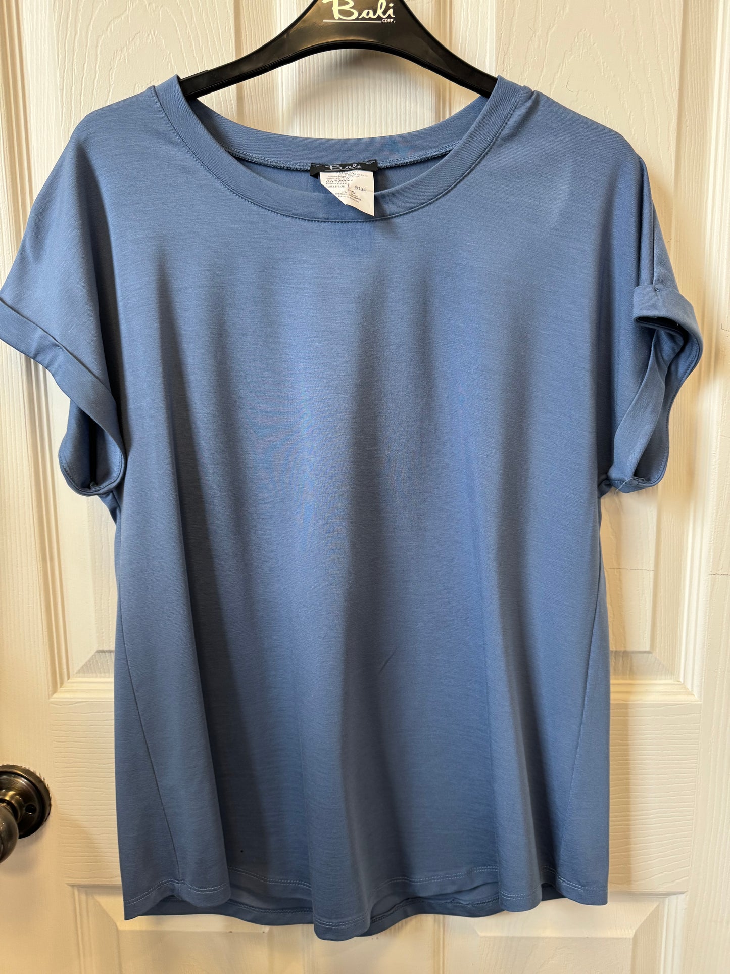 A Bali Crewneck T-Shirt - BLUE 8134 by Bali Corp hangs on a black hanger with the word "Bali" on it. The shirt, made in Canada, has a round neckline and is displayed against a white background, likely a door. The sleeves are rolled up slightly, and a small tag is visible at the neckline.