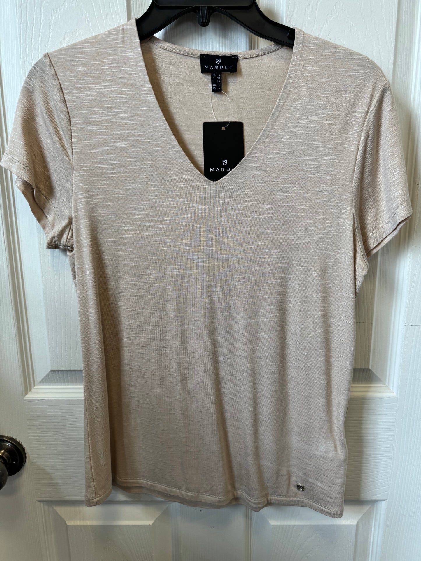 A Marble Fitted V-Neck T-Shirt - BEIGE 6539 is displayed on a black hanger against a white door. The shirt has a fitted silhouette, subtle marbled texture, and features a black rectangular tag with the brand name "MARBLE," along with a smaller label on the left bottom hem.