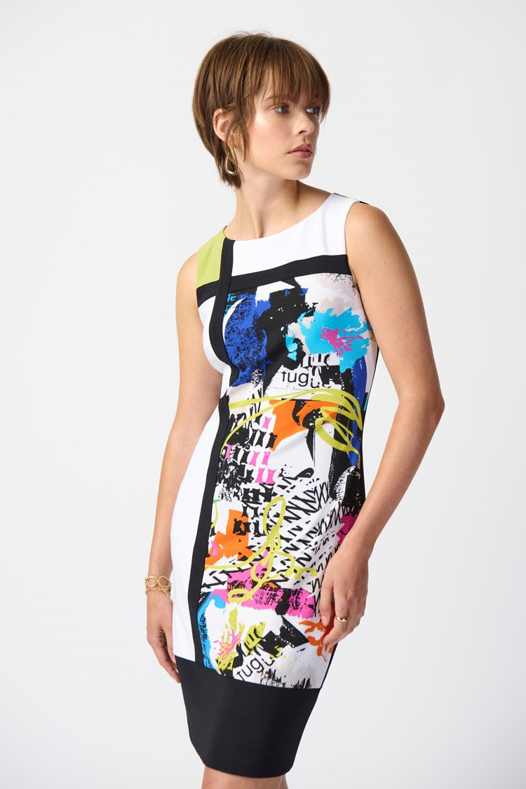 A woman with short hair stands against a plain background, wearing the Joseph Ribkoff - Abstract Print Silky Knit Sheath Dress 241296. Complementing her outfit, she has on black, open-toe heels. One hand rests by her side while the other is slightly extended.