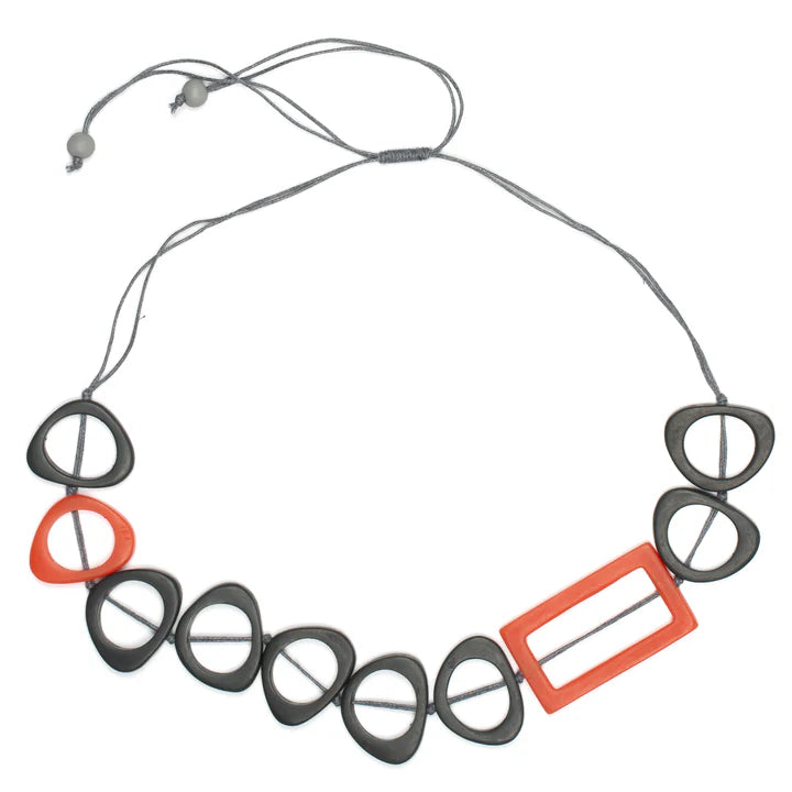 The Resin Rectangular Hoop Necklace by Suzie Blue is a modern accessory featuring a sleek rectangular hoop design with a thin grey cord and adjustable bead ends. It showcases black and orange angular geometric shapes, incorporating unique resin material, with one large rectangular orange piece and alternating black triangle-like figures, including one in orange.