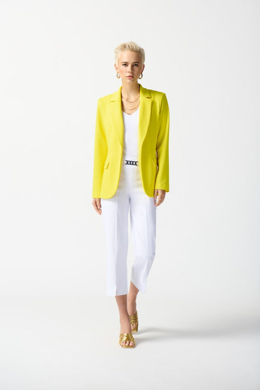 A person with short blonde hair is wearing a bright yellow blazer over a white top, Millennium Straight Crop Pants 242035 from Joseph Ribkoff, and matching yellow shoes. They accessorize with gold earrings and a necklace and have a calm expression while posing against a plain white background.