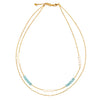 The Double Strand Necklace With Crystal Beads by Suzie Blue is a handmade gold chain piece featuring small white and blue beads arranged in clusters. This delicate necklace includes an adjustable clasp at the back for customizable length, enhancing its simple yet elegant design.