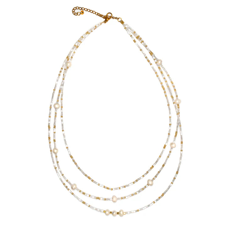 Introducing the **Triple Strand Necklace With Pearls** from **Suzie Blue**: A delicate, handmade necklace featuring three strands of small white and gold beads interspersed with lustrous pearls. The varying lengths of the strands create an elegant layered effect, and it is finished with a gold lobster clasp and a short gold chain for adjustable length.