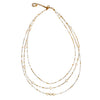 Introducing the **Triple Strand Necklace With Pearls** from **Suzie Blue**: A delicate, handmade necklace featuring three strands of small white and gold beads interspersed with lustrous pearls. The varying lengths of the strands create an elegant layered effect, and it is finished with a gold lobster clasp and a short gold chain for adjustable length.