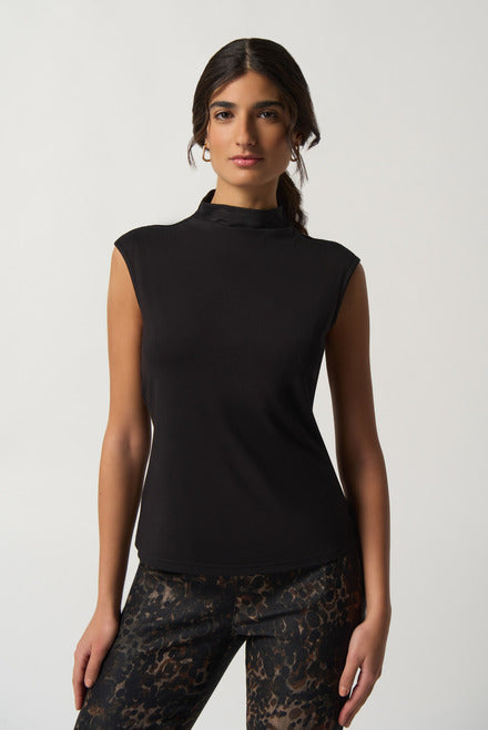 A woman with long, dark hair stands against a plain background, wearing a Joseph Ribkoff Mock Neck Top Style 233230 in black, made from luxurious jersey knit fabric and patterned pants. She has a neutral expression and wears hoop earrings.