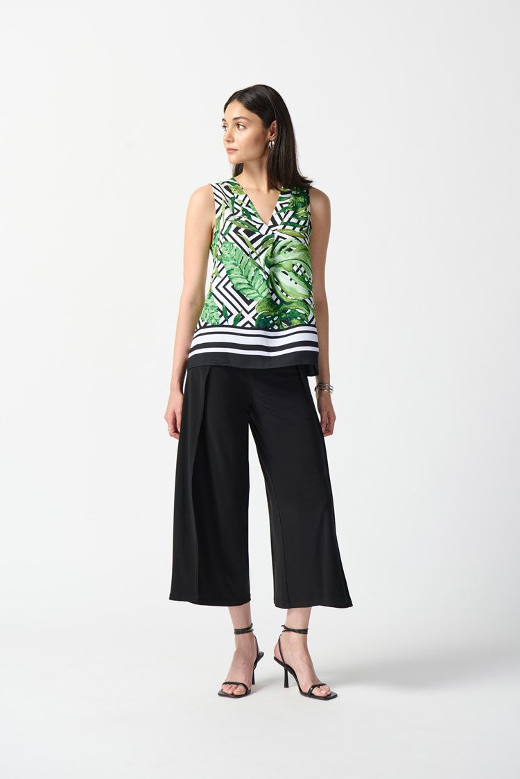 A woman wearing a Woven Tropical Print Flared Top 242237 from Joseph Ribkoff, featuring a vibrant Vanilla and Multi-color pattern with black and white geometric designs. Her outfit is paired with black wide-leg trousers and black high-heeled sandals. She is looking to the side against a plain white background.