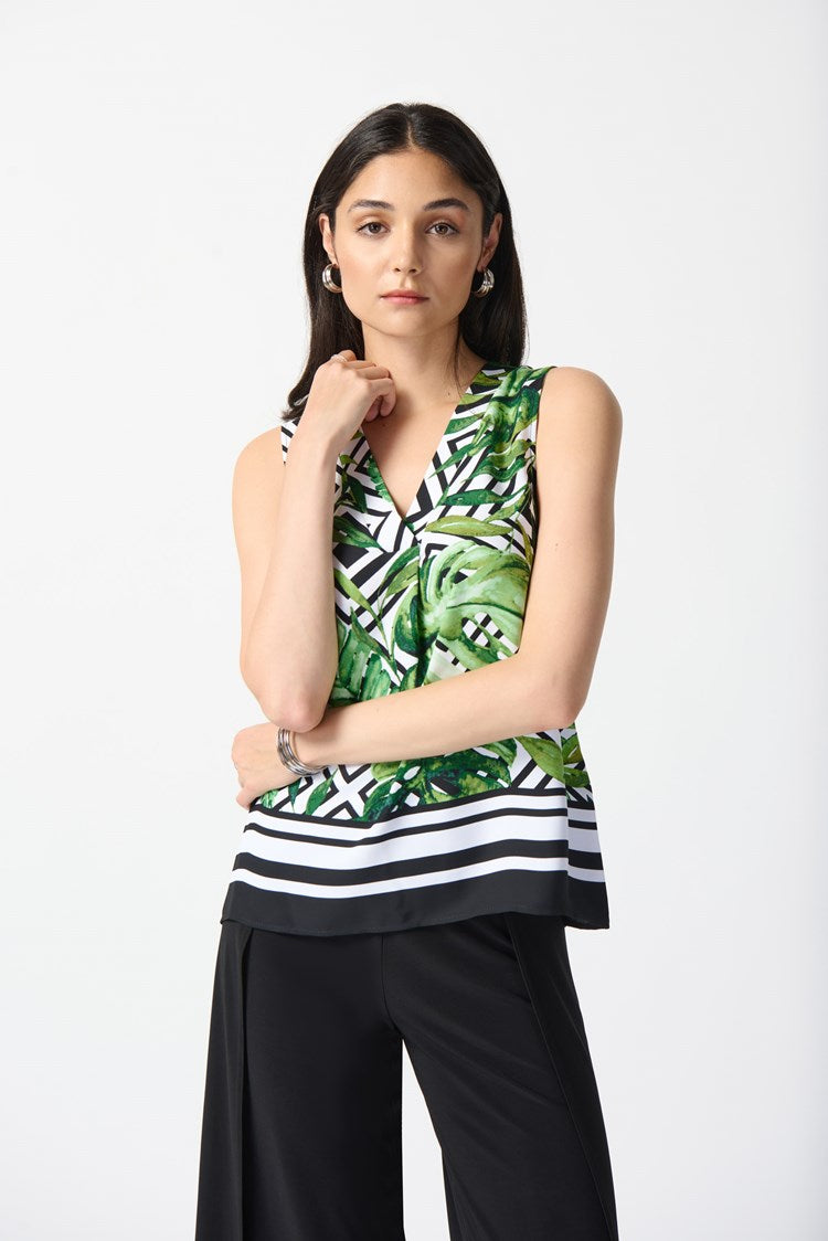 A woman wearing a Woven Tropical Print Flared Top 242237 from Joseph Ribkoff, featuring a vibrant Vanilla and Multi-color pattern with black and white geometric designs. Her outfit is paired with black wide-leg trousers and black high-heeled sandals. She is looking to the side against a plain white background.