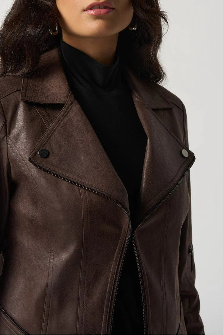 A woman with long, wavy dark hair wears the Joseph Ribkoff Pleather Moto Jacket - Style 233969 over a black turtleneck. She stands with a confident expression and her hands down by her sides, against a plain light-colored background.