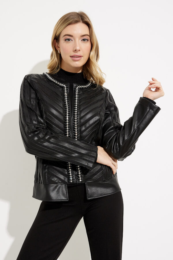 A woman with light hair wears the Joseph Ribkoff Studded Collarless Jacket 233969, a black, striped, textured leather piece featuring bead embellishments and zipper pockets. She pairs it with a black top and black pants while posing against a plain white background, looking straight ahead with one hand on her hip and the other slightly raised.