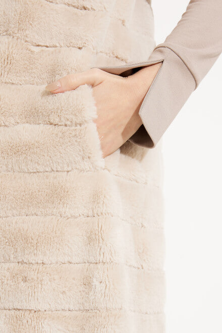 Close-up of a person's hand tucked into the pocket of a Joseph Ribkoff Faux Fur Longline Vest, Style 233924. The luxurious beige vest features horizontal ribbed patterns. The person is wearing a long-sleeve beige top that partially covers the wrist. The image has a clean, white background.