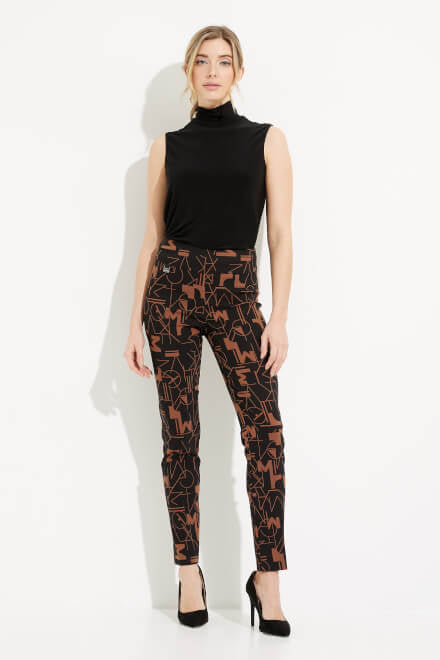 A person wearing the Abstract Print Straight Leg Pants Style 233279 by Joseph Ribkoff, featuring a black high-waisted design with an abstract brown geometric pattern, paired with a black top and black high heels, stands against a white background with one hand on their hip.