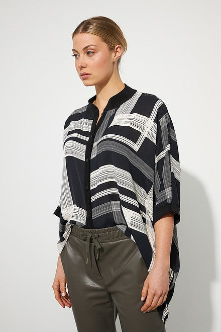 A woman stands against a plain white background, wearing a black and white geometric patterned top with three-quarter sleeves. She pairs it with Joseph Ribkoff's Faux Leather Joggers Style 223166 in Avocado and black ankle boots, with her hair pulled back.