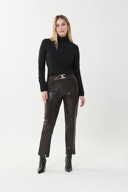 A woman stands against a plain white background, dressed in a black turtleneck sweater, Joseph Ribkoff's Style 223131 MOCHA faux leather pants featuring a metallic waist buckle, and black heeled boots. She has straight blonde hair and gazes directly at the camera with a neutral expression.