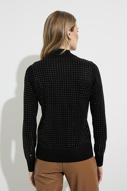 A woman with long, wavy blond hair stands against a plain white background. She is wearing a Joseph Ribkoff Embellished Mock Neck Style 224945 BLACK sweater paired with light brown pants. Her arms are crossed, and she has a neutral expression.