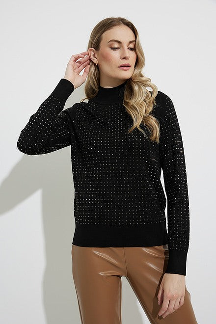 A woman with long, wavy blond hair stands against a plain white background. She is wearing a Joseph Ribkoff Embellished Mock Neck Style 224945 BLACK sweater paired with light brown pants. Her arms are crossed, and she has a neutral expression.