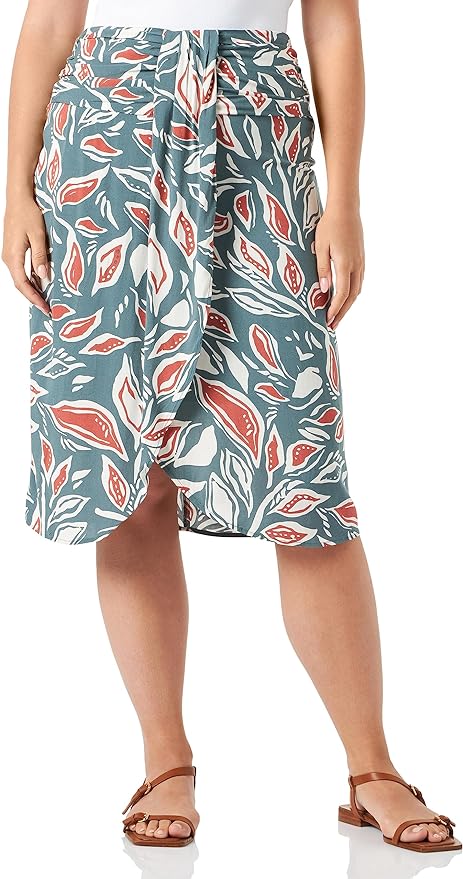 A person is shown from the back wearing the SoyaConcept Sc-LEDA 2 Women's Skirt, featuring a bold, leafy pattern in green, red, and white. The knee-length skirt offers a comfortable fit and is paired with a sleek white top and brown sandals on a crisp white background.