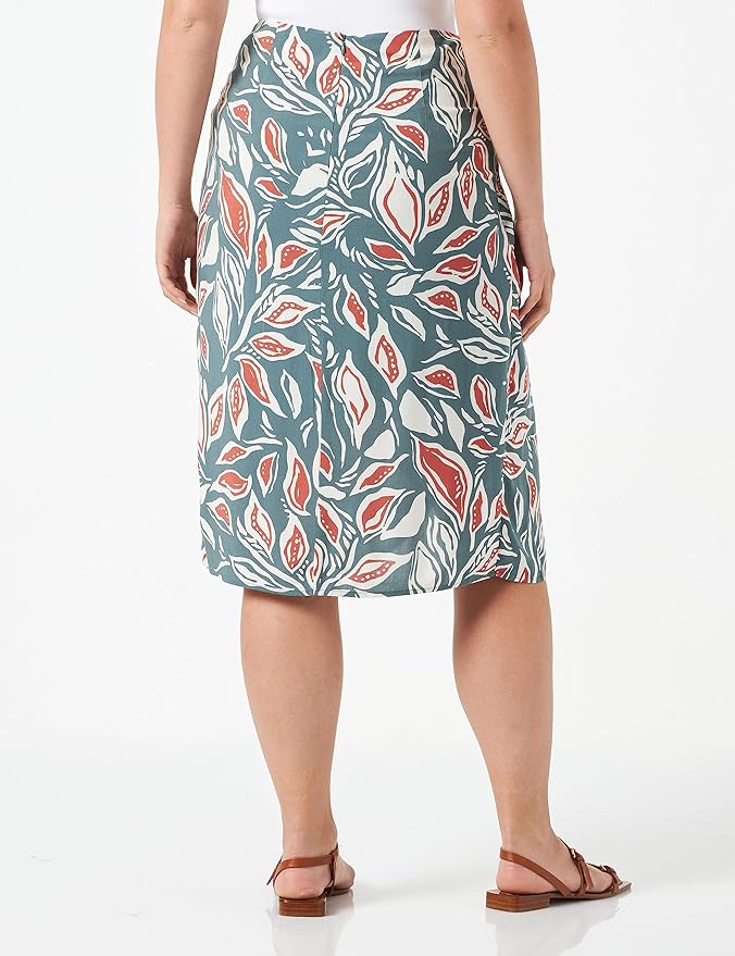 A person is shown from the back wearing the SoyaConcept Sc-LEDA 2 Women's Skirt, featuring a bold, leafy pattern in green, red, and white. The knee-length skirt offers a comfortable fit and is paired with a sleek white top and brown sandals on a crisp white background.