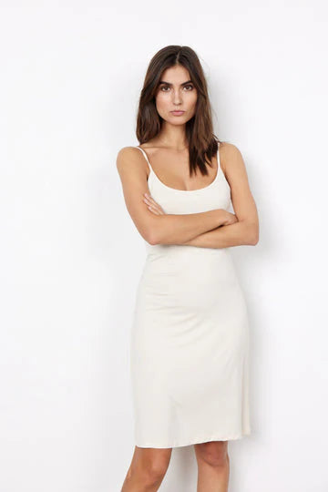 A woman with long brown hair is wearing a sleeveless, knee-length, off-white SC-MARICA 62 Tank Dress by SoyaConcept. She stands against a plain white background with her arms crossed, looking directly at the camera, making a stylish choice with this versatile dress.