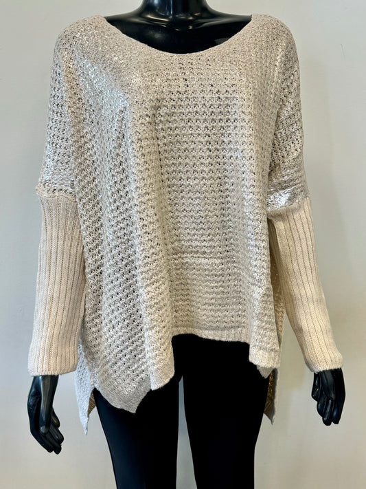 Displayed on a black mannequin, the Knit Sweater Sparkle - ETERNELLE by ETERNELLE is a beige, loose-knit sweater with ribbed sleeves. Perfect for your winter wardrobe, this sweater features a wide, round neckline and a high-low hemline, where the back is slightly longer than the front. The open and airy pattern gives it a casual look.