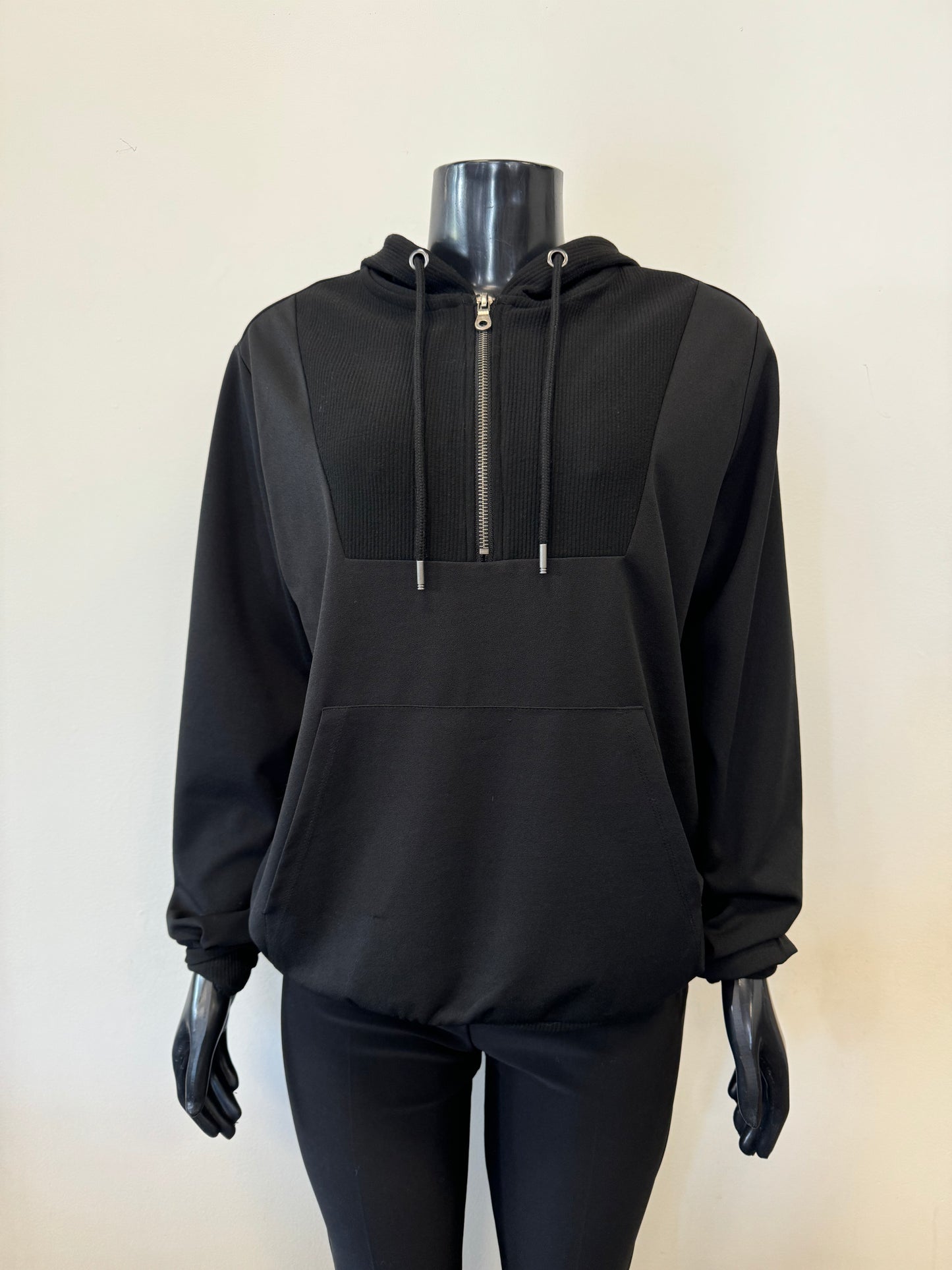 The SoyaConcept Hooded Sweat Black is displayed on a black, headless mannequin. This hoodie, crafted from recycled polyester, features a front zipper, drawstrings, a textured panel on the chest, and a front pocket. The mannequin is also dressed in black pants to complete the sustainable monochromatic outfit against a plain background.