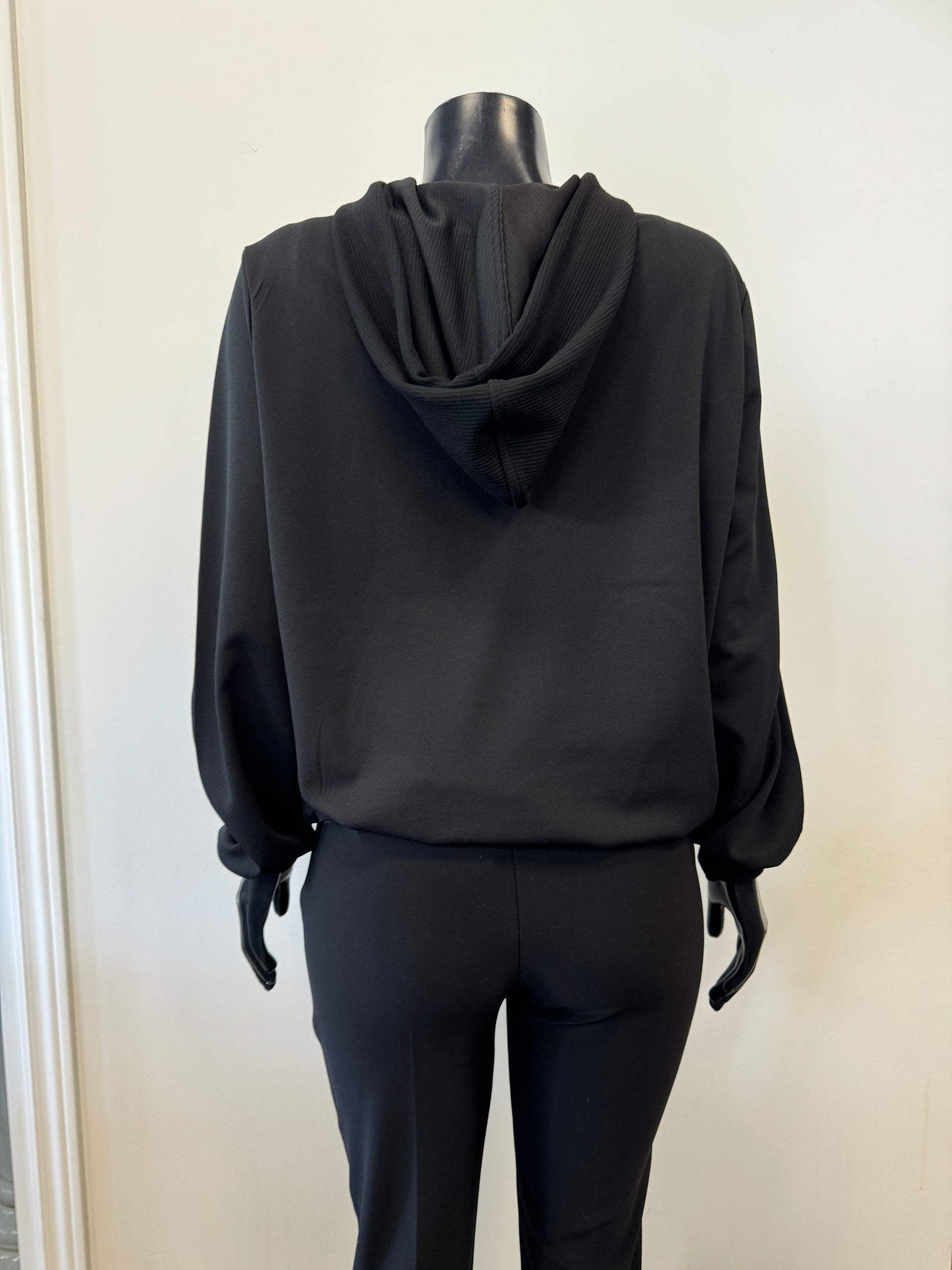 The SoyaConcept Hooded Sweat Black is displayed on a black, headless mannequin. This hoodie, crafted from recycled polyester, features a front zipper, drawstrings, a textured panel on the chest, and a front pocket. The mannequin is also dressed in black pants to complete the sustainable monochromatic outfit against a plain background.